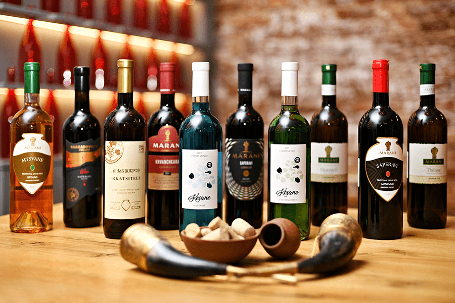 Assorted wine bottles lined up on a wooden bar with corks and tobacco pipes in the foreground.